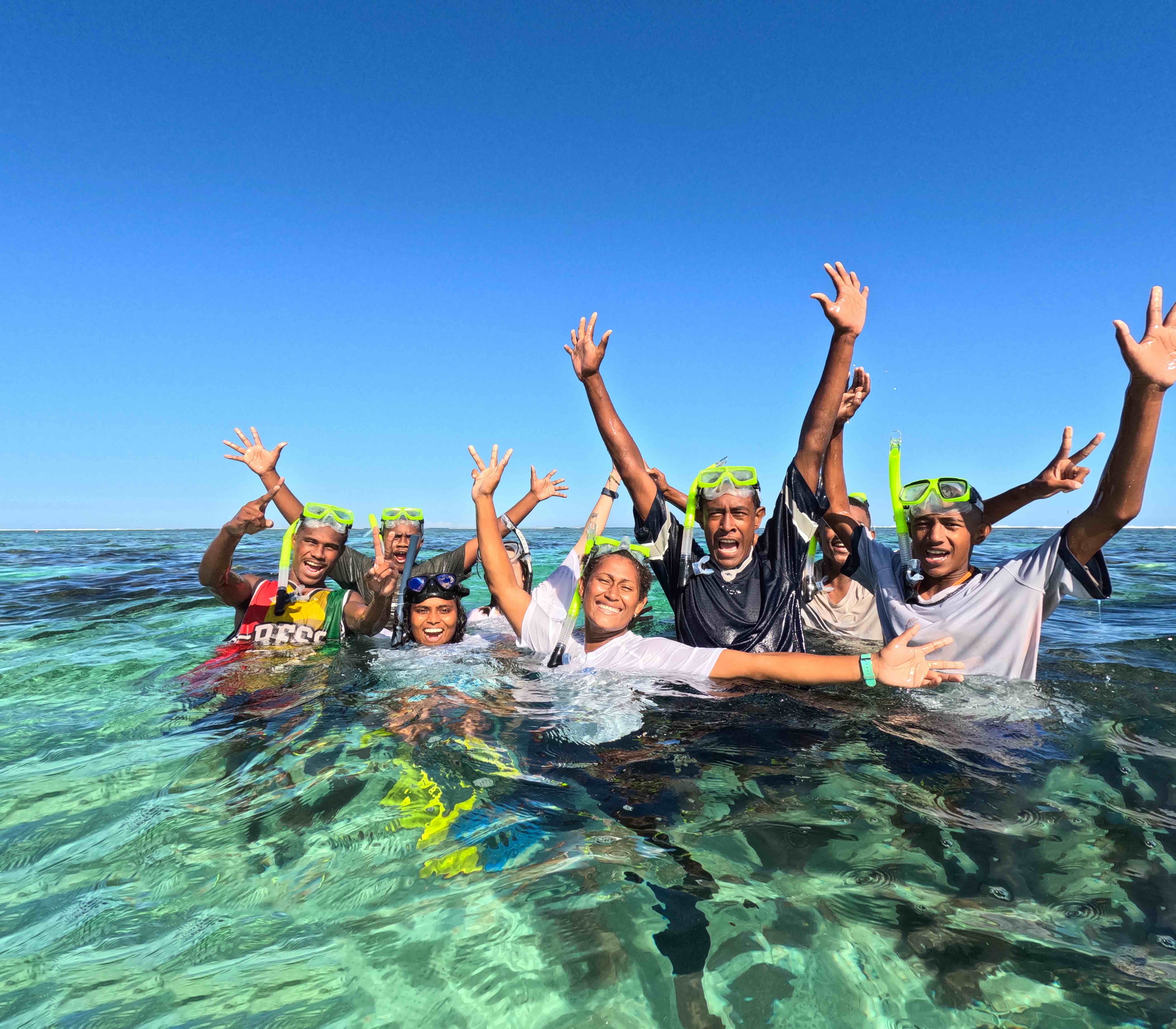 A group of happy snorkellers posing for the camera in the crystal clear waters of Fiji's Naidiri Marine Biodiversity Park